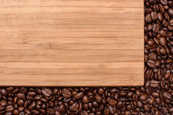 Um fundo de madeira ao redor das bordas polvilhado com café de grão torrado, espaço para texto — Fotografia de Stock