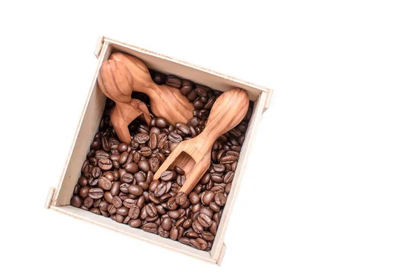 Grilled fragantes granos de café se encuentran en una caja de madera, en una caja se encuentran cucharadas de olivar con granos de café, aislados sobre un fondo blanco — Foto de Stock
