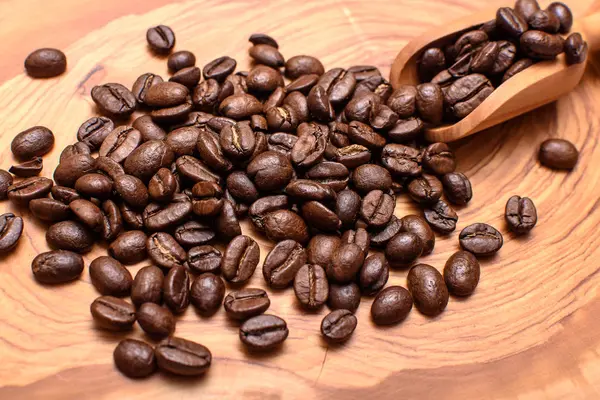Los granos de café tostados se encuentran en la superficie de madera de olivo con una cucharada — Foto de Stock