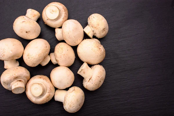 Целые грибы шампиньоны целая ложь на черном камне шифер, фон — стоковое фото