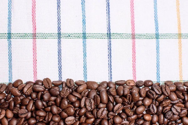 Textura de uma toalha colorida, uma toalha de um tipo celular, em que reside uma certa quantidade de grãos de café marrom. Vista superior com um monte de grãos de café com espaço para texto — Fotografia de Stock