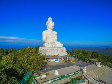 Phuket Big Buddha heykeli dağın tepesinde arkasında sahne mavi gökyüzü ve mavi okyanus vardır.
