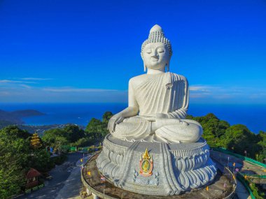 Phuket Big Buddha heykeli dağın tepesinde arkasında sahne mavi gökyüzü ve mavi okyanus vardır.