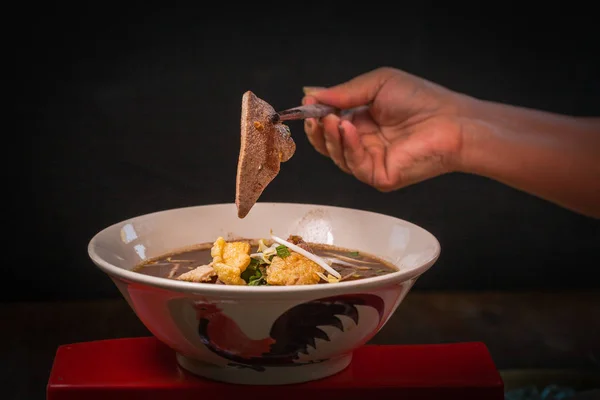 Hand uses chopsticks to pickup tasty noodles on black background