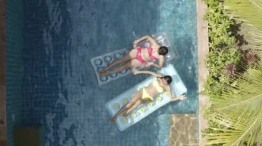 Kırmızı bikinili iki kadın ve yüzme havuzunda sarı bikinili iki kadın.