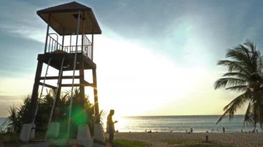Gün batımında Karon Sahili Phuket 'te yürüyen ve fotoğraf çeken bir adam. Karon sahilindeki cankurtaran kulesinde gün batımı. 