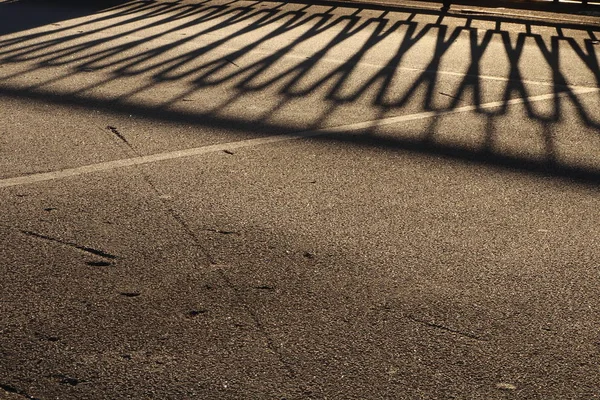Balustrada zabezpieczająca cień na oblodzonej drodze asfaltowej powierzchni. Urban tło ulica — Zdjęcie stockowe