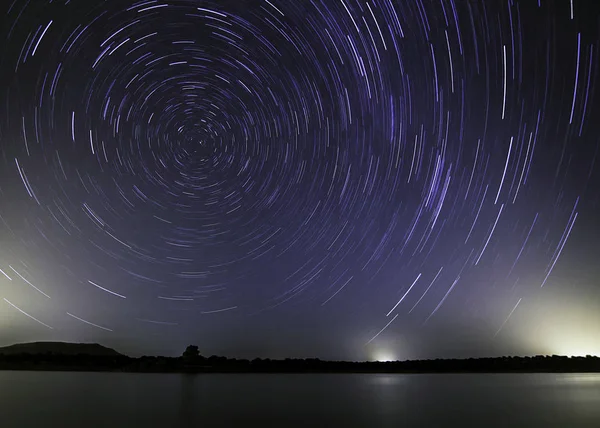 Sky with a trail of stars revolving on the polar star indicating where north is on a lake.                          The lake and the polar star.