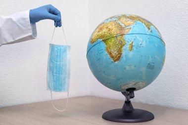 Dünya gezegeninin yanında bir el maske tutuyor.