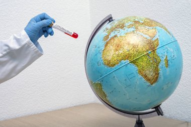 Bir el, Dünya gezegeninin yanında bir test tüpü ve bir covid-19 örneği tutuyor.