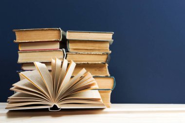 Açık kitap, ahşap masa üzerinde ciltli kitap yığını.