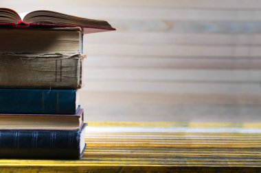 Açık kitap, ahşap masa üzerinde ciltli kitap yığını.