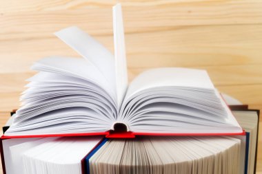 Açık kitap, ahşap masa üzerinde ciltli kitap yığını.