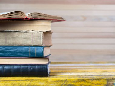 Açık kitap, ahşap masa üzerinde ciltli kitap yığını.