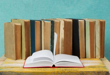 Açık kitap, ahşap masa üzerinde ciltli kitap yığını.