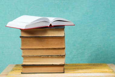 Açık kitap, ahşap masa üzerinde ciltli kitap yığını.