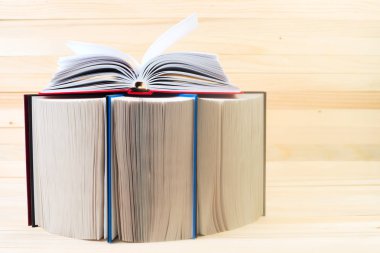 Açık kitap, ahşap masa üzerinde ciltli kitap yığını.