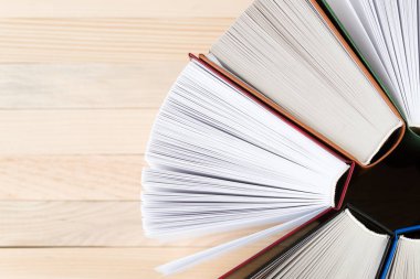 Açık kitap, ahşap masa üzerinde ciltli kitap yığını.