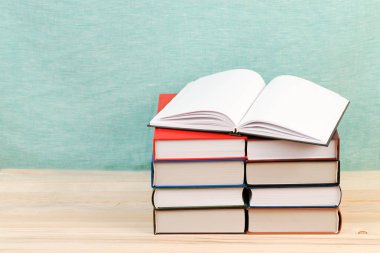 Açık kitap, ahşap masa üzerinde ciltli kitap yığını.