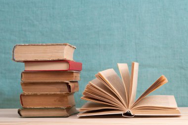 Açık kitap, masada ciltli kitap yığını.