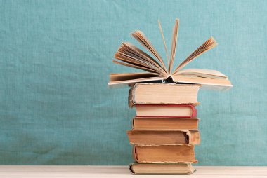 Açık kitap, masada ciltli kitap yığını.