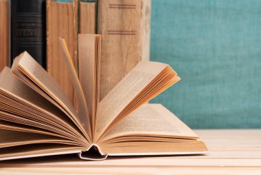 Açık kitap, masada ciltli kitap yığını.