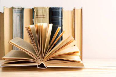 Açık kitap, masada ciltli kitap yığını.