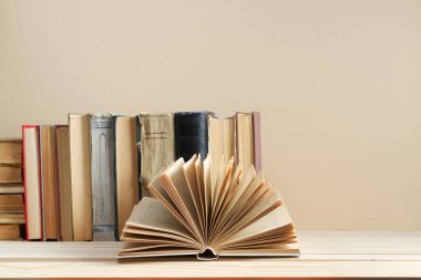 Açık kitap, masada ciltli kitap yığını.