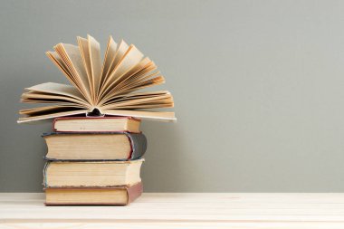 Açık kitap, masada ciltli kitap yığını.