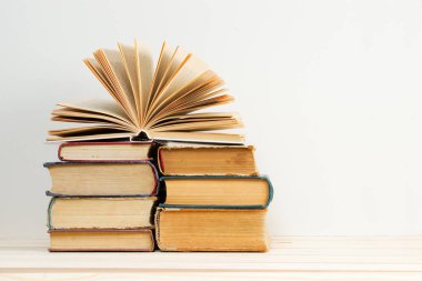 Açık kitap, masada ciltli kitap yığını.