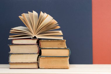 Açık kitap, masada ciltli kitap yığını.