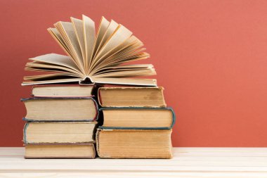 Açık kitap, masada ciltli kitap yığını.