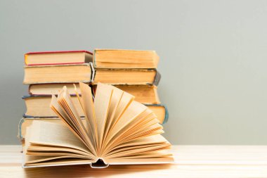 Açık kitap, masada ciltli kitap yığını.
