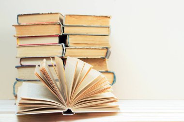Açık kitap, masada ciltli kitap yığını.