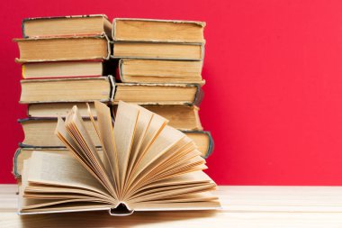 Açık kitap, masada ciltli kitap yığını.