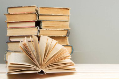 Açık kitap, masada ciltli kitap yığını.