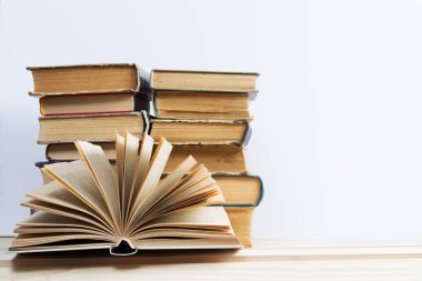 Açık kitap, masada ciltli kitap yığını.
