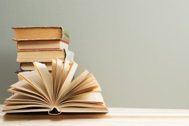 Açık kitap, masada ciltli kitap yığını.