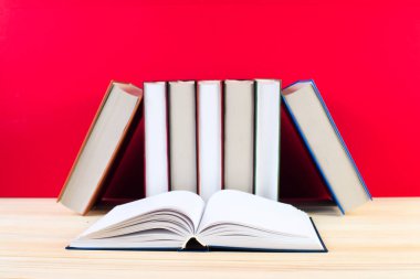 Açık kitap, ahşap masa üzerinde ciltli kitap yığını.