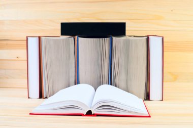 Açık kitap, ahşap masa üzerinde ciltli kitap yığını.