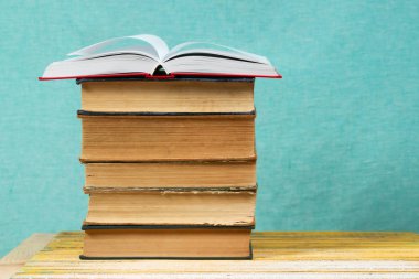 Açık kitap, ahşap masa üzerinde ciltli kitap yığını.