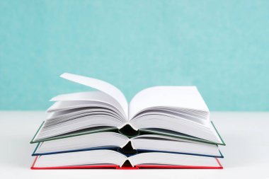 Açık kitap, masada ciltli kitap yığını.