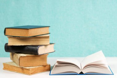 Açık kitap, masada ciltli kitap yığını.