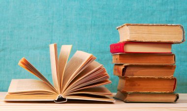 Açık kitap, ahşap masa üzerinde ciltli kitap yığını.