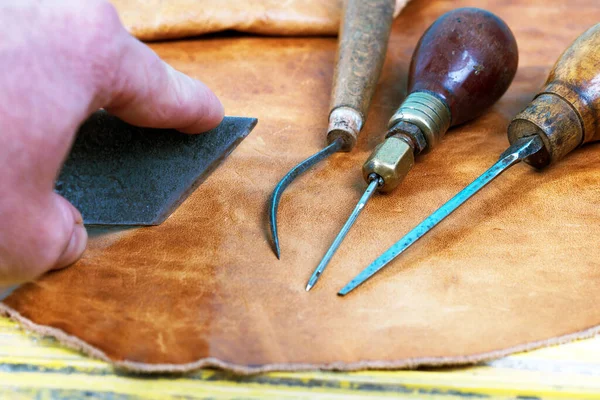 Шкіряні інструменти для ремесел на дерев'яному тлі. Шкіряні майстри працюють на робочому столі. Шматок хованки та робочі інструменти ручної роботи на робочому столі — стокове фото