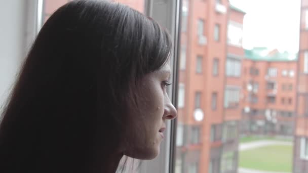 La chica cuidadosamente mira por la ventana — Vídeo de stock
