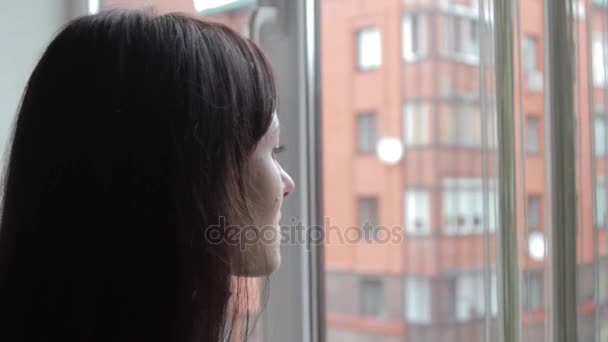 A menina olha atenciosamente pela janela — Vídeo de Stock