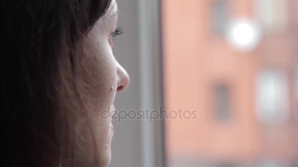 La chica mira por la ventana y recuerda algo. — Vídeos de Stock