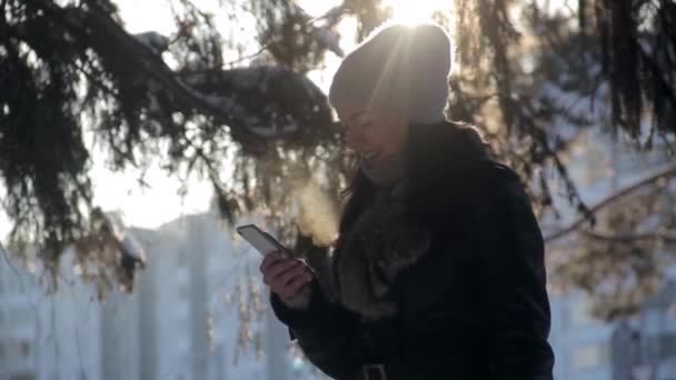 Девушка пользуется смартфоном зимой — стоковое видео