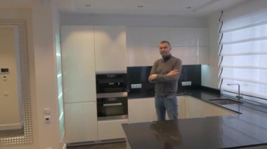 Genç bir adam mutfakta duruyor ve kameraya bakıyor